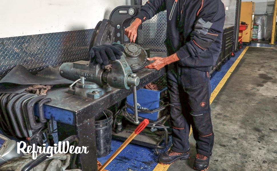 Man wearing PolarForce Pants, sweatshirt and boots in a mechanics shop
